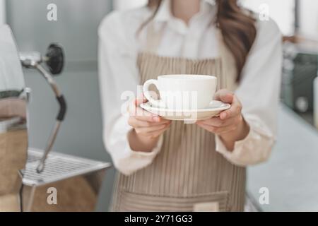 Fermez les mains d'une barista tenant une tasse de café pour servir sa cliente Banque D'Images