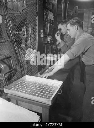 "Accélérer la production à la Royal Mint." La délivrance des médailles du Service général aux anciens militaires s'accélère et, à la monnaie royale, la frappe de 12 000 000 médailles de guerre en cupro-nickel a déjà commencé avec un objectif de 500 000 médailles par mois. Le roi a approuvé la conception le mois dernier. L'image montre : 'Trayful of Treasure' - Mr.C. Ley (caméra la plus proche) guide une rangée de nouvelles médailles de guerre du service général, tandis que M. A. Hodge les inspecte à la monnaie royale, aujourd'hui. 16 mars 1948. Banque D'Images