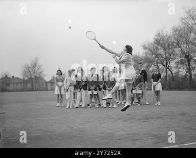 24 garçons et filles, entre 10 et 18 ans, suivent des cours spéciaux de tennis sur gazon au Sundridge Park Club (kent), sur un parcours junior de six à l'invitation du club. Des conférences et des manifestations sur les différents coups sont données par M. J. E Pryor, un entraîneur de Kent, et M. C. B Dniels, le capitaine du club. Images : Ann Miller-Hallett, 17 ans, monte pour rendre un cliché, sous les yeux de camarades élèves à Sundridge Park, aujourd'hui (mercredi). 14 avril 1948. Banque D'Images