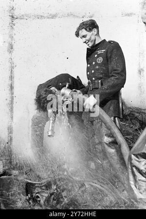 Les brigades de pompiers de toute la banlieue sud ont combattu un incendie féroce dans la plus grande décharge en caoutchouc de Londres, à Carshalton Road, Mitcham Junction. Des milliers de tonnes de déchets de caoutchouc ont brûlé rapidement alors que les pompiers se battaient pour que l'eau joue sur l'incendie. Le manque d'eau a gravement handicapé les efforts visant à maîtriser les flammes. Une usine voisine aurait été allumée, et des bandes d'hommes travailleraient pour dégager une « rupture » de la scène de la décharge et des maisons voisines. Le feu a fourni la plus spectaculaire poussée de fumée sur la capitale depuis les pires jours du blitz. Images : une façon de se rafraîchir après avoir gardé le fi Banque D'Images