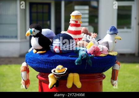 Un chapeau en laine tricoté coloré original avec un thème de bord de mer, des oiseaux de mer crochetés et d'autres créatures marines décore une boîte pilier rouge britannique traditionnelle. Banque D'Images