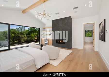 Cette chambre moderne avec de grandes fenêtres, du parquet et une cheminée offre une vue panoramique sur la végétation luxuriante à l''extérieur. Banque D'Images