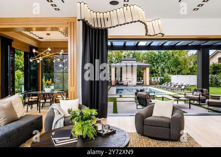 Ce salon luxueux et moderne offre une vue sur une élégante piscine extérieure et sur le jardin. Il dispose d''un mobilier contemporain et d''un éclairage élégant. Banque D'Images