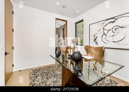 Bureau à domicile moderne avec bureau en verre, art abstrait et tapis confortable, avec lumière naturelle des fenêtres. Banque D'Images