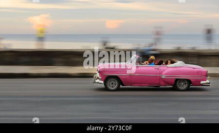 745 panoramique image de voiture classique américaine rose -Chevrolet 1953- conduite sur la promenade Malecon, les gens locaux sur le parapet du front de mer. La Havane-Cuba. Banque D'Images