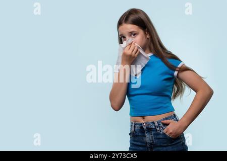 Une jeune fille s'essuyant le nez avec un mouchoir, montrant des signes de rhume ou d'allergie dans un studio. Banque D'Images