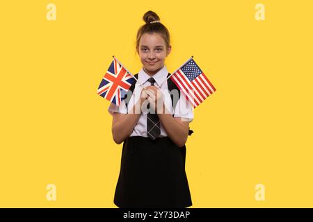 Une écolière tient les drapeaux britannique et américain, souriant avec confiance. Banque D'Images