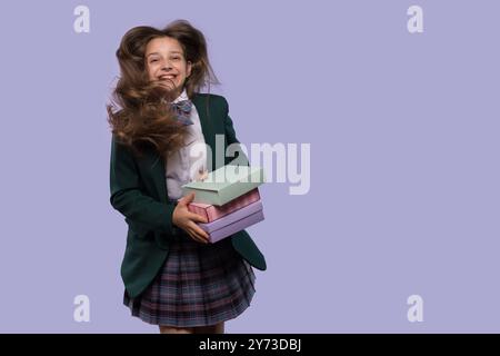 Une écolière riante tient des boîtes-cadeaux colorées avec ses cheveux soufflant dans le vent. La fille saute de joie Banque D'Images