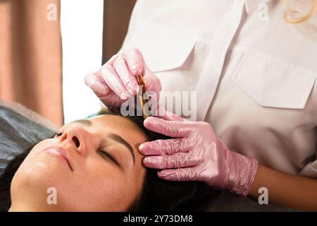 Une esthéticienne applique un sérum sur le front d’un client pendant un traitement du visage. Banque D'Images