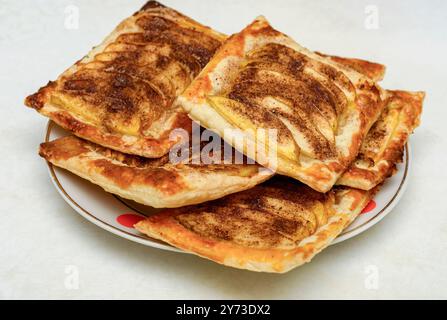 Une assiette de pâtisseries aux pommes fraîchement cuites avec garniture à la cannelle, sur fond blanc. Concept de desserts et pâtisseries maison Banque D'Images