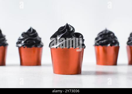 Cupcakes orange avec tourbillon noir de crème au beurre, cupcakes dans des doublures de feuille orange avec crème au beurre noir, cupcakes d'Halloween givrés sur un fond blanc Banque D'Images