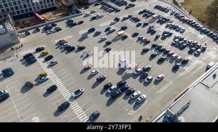 Vue aérienne d'un grand parking rempli de diverses voitures garées. Le lot a marqué des places de parking et est partiellement vide, avec un mélange de couleurs et Banque D'Images