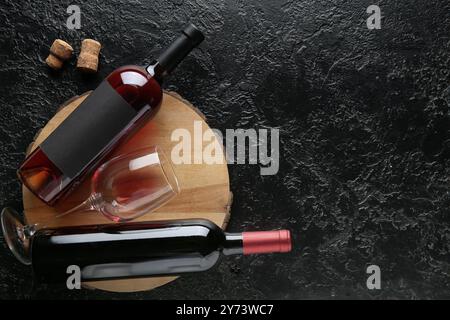 Plateau en bois avec bouteilles de vin rouge et verre sur fond grunge noir Banque D'Images