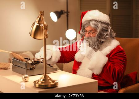 Père Noël avec machine à écrire buvant du lait tout en écrivant l'histoire de Noël la nuit Banque D'Images