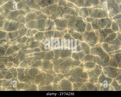 La texture du sable et les reflets de lumière sur l'eau doucement ondulée. Surface de l'eau ondulée. Banque D'Images