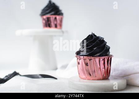 Glaçage noir sur cupcakes roses avec un fond blanc, cupcakes en feuilles roses avec crème au beurre noire Banque D'Images