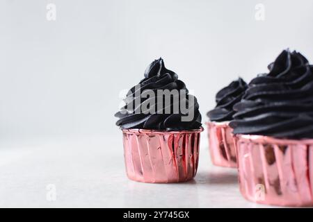 Glaçage noir sur cupcakes roses avec un fond blanc, cupcakes en feuilles roses avec crème au beurre noire Banque D'Images