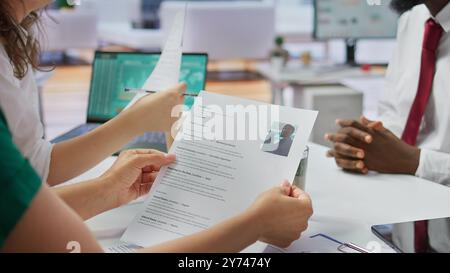 Le candidat remet son CV à une équipe de professionnels des RH afin de commencer l'entretien, en se concentrant sur l'expérience dans le CV. Discuter du développement de carrière potentiel. Gros plan. Caméra B. Banque D'Images
