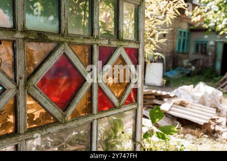 Fenêtre en verre magnifiquement vieilli avec des vitres colorées encadrant une scène de jardin rustique. Banque D'Images