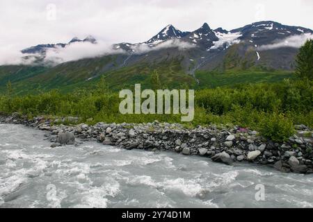 Un ruisseau glaciaire coulant à travers une vallée de l'Alaska avec de la neige sur les montagnes. Banque D'Images