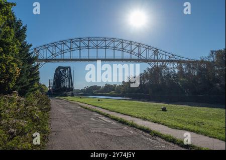 Pont international enjambe le canal. Soleil levant lumineux au-dessus du pont et un pont tournant ferroviaire est vu ci-dessous. Les arbres bordent les deux côtés. Banque D'Images