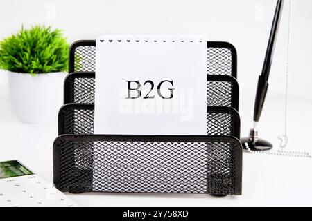 B2G - abréviation de Business to Government. B2G écrit sur une feuille de papier blanche dans un support de papeterie sur un fond blanc Banque D'Images