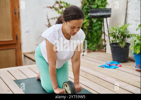 Une femme s'engageant dans une séance de yoga à l'extérieur en utilisant une roue d'exercice, favorisant la santé et le bien-être par une journée ensoleillée. Banque D'Images