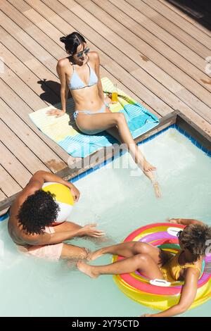 Détente au bord de la piscine, amis divers profitant de la journée d'été avec des boissons et des flotteurs de piscine, à la maison Banque D'Images