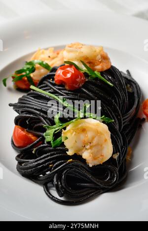 Spaghetti al Nero di Seppia con Gamberi, pâtes italiennes à l'encre de calmar, crevettes, tomates et rocola Banque D'Images