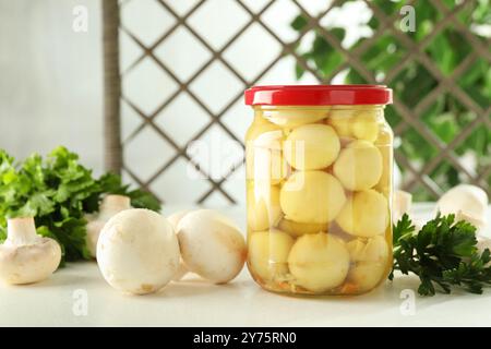 Savoureux champignons marinés en pot et persil sur table blanche à l'intérieur Banque D'Images