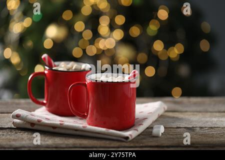 Savoureuse boisson chaude au cacao avec des cannes en sucre et des guimauves dans des tasses rouges sur une table en bois Banque D'Images