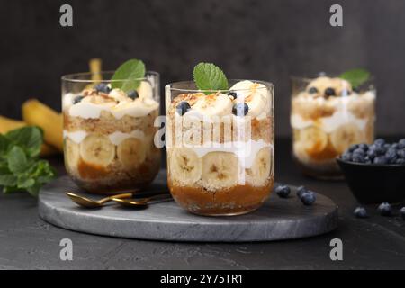 Dessert savoureux à base de bagatelle. Génoise, bleuets, banane et crème fouettée dans des verres sur table noire Banque D'Images