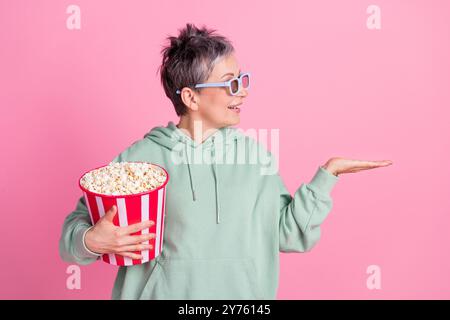 Photo de drôle de bonne humeur Lady Wear kaki Hoodie Watch film manger pop corn tenant le bras vide espace isolé fond de couleur rose isolé Banque D'Images