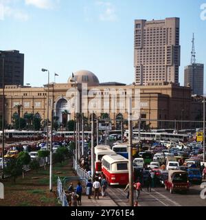 Tägliches Verkehrschaos auf der Meret Basha Straße mit Blick auf das Ägyptische Museum (Kuppel) und den Ramses Hotelturm in Kairo, nahe vom Midan al Tahrir Platz, Ägypten um 1987. Banque D'Images