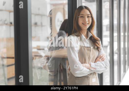 Heureuse jeune femme propriétaire de café debout à l'extérieur de son magasin croisant ses bras souriant à la caméra Banque D'Images