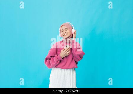 Une jeune femme insouciante aime la musique dans un pull rose élégant sur un fond bleu vif Banque D'Images