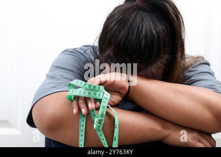 Triste femme asiatique triste parce que le régime Unsuccès, Fat bouleversement ennuyé de régime perte de poids échouer. Ruban de mesure de maintien. Banque D'Images