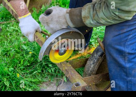 À l'aide d'une scie à main de meuleuse d'angle, l'ouvrier coupe des cadres métalliques Banque D'Images