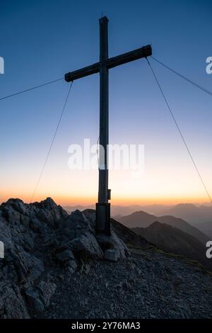 Le sommet croise sur le mont Hinteres Sonnwendjoch contre la lumière colorée de l'aube, Tyrol, Autriche Banque D'Images