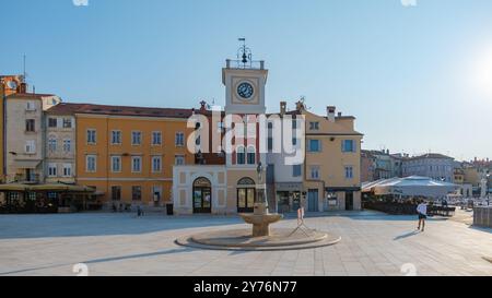 Rovinj Croatie 27 août 2024, le soleil baigne la place dans la chaleur tandis que les gens se promènent devant des bâtiments colorés et la tour de l'horloge emblématique. Les cafés extérieurs invitent les visiteurs à profiter de l'atmosphère agréable. Banque D'Images