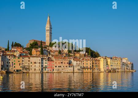 La charmante ville côtière de Rovinj prend vie au coucher du soleil, avec des bâtiments aux couleurs pastel bordant le front de mer et reflétant magnifiquement dans la mer Adriatique calme, créant une scène pittoresque. Banque D'Images