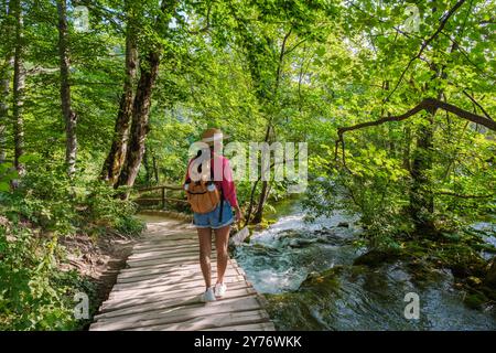 Un voyageur serpente le long d'un chemin en bois entouré de verdure vibrante et d'eaux en cascade, immergé dans la beauté enchanteresse du parc national des lacs de Plitvice en Croatie. Banque D'Images