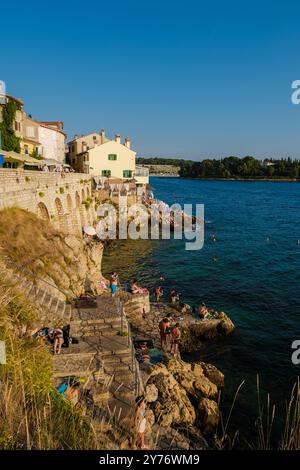 Rovinj Croatie 27 août 2024,les visiteurs profitent d'une journée ensoleillée au front de mer rocheux de Rovinj, avec des gens se prélassant, nageant et profitant de la vue imprenable sur la mer Adriatique Banque D'Images