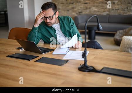 Comptable masculin stressé avec la tête dans les mains lisant des e-mails sur ordinateur portable tout en travaillant au bureau dans le bureau Banque D'Images