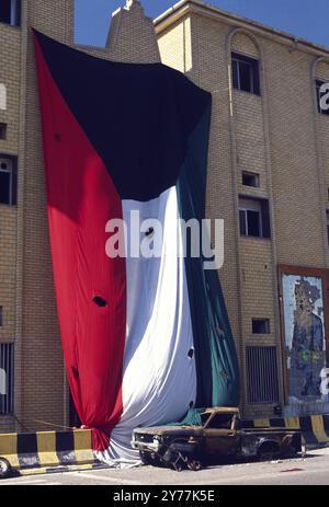 Première Guerre du Golfe : 8 mars 1991 Un immense drapeau du Koweït, percé de trous d'obus, à côté d'un grand portrait carrelé de Saddam Hussein abîmé par des balles. C'est sur le mur d'un bâtiment, une partie du Seif Palace, maison de l'émir à Koweït City. Banque D'Images