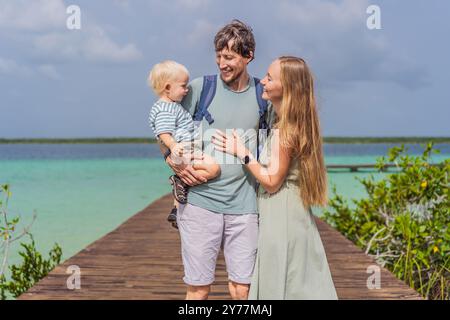 Maman, papa et leur bébé fils explorant la jetée en bois au-dessus des eaux turquoises du lac Bacalar, au Mexique. Concept de destination de voyage tropical paisible Banque D'Images