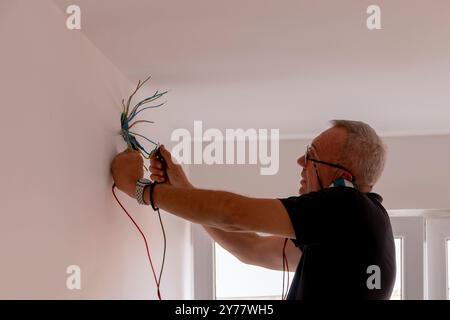 Électricien, examine la connexion du câble dans la ligne électrique. Le technicien tire le fil du conduit sur le chantier. Constructeur au travail, examine conne Banque D'Images