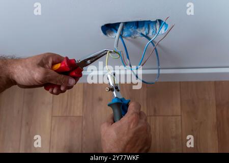 Électricien, examine la connexion du câble dans la ligne électrique. Le technicien tire le fil du conduit sur le chantier. Constructeur au travail, examine conne Banque D'Images