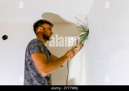 Électricien, examine la connexion du câble dans la ligne électrique. Le technicien tire le fil du conduit sur le chantier. Constructeur au travail, examine conne Banque D'Images