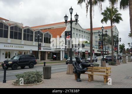 Rue principale avec sculpture de vache, palmiers, voitures et bâtiments avec des boutiques de luxe à Oranjestad à Aruba. Banque D'Images